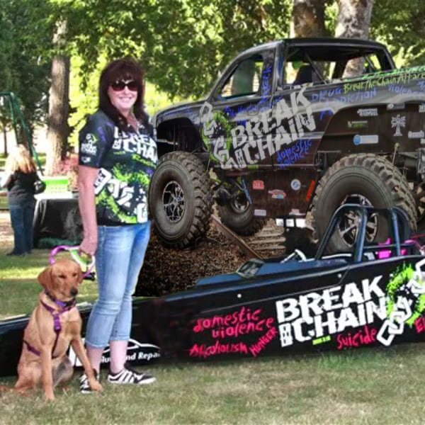 Tammi Burns standing next to a dragster and truck with her dog on a sunny day
